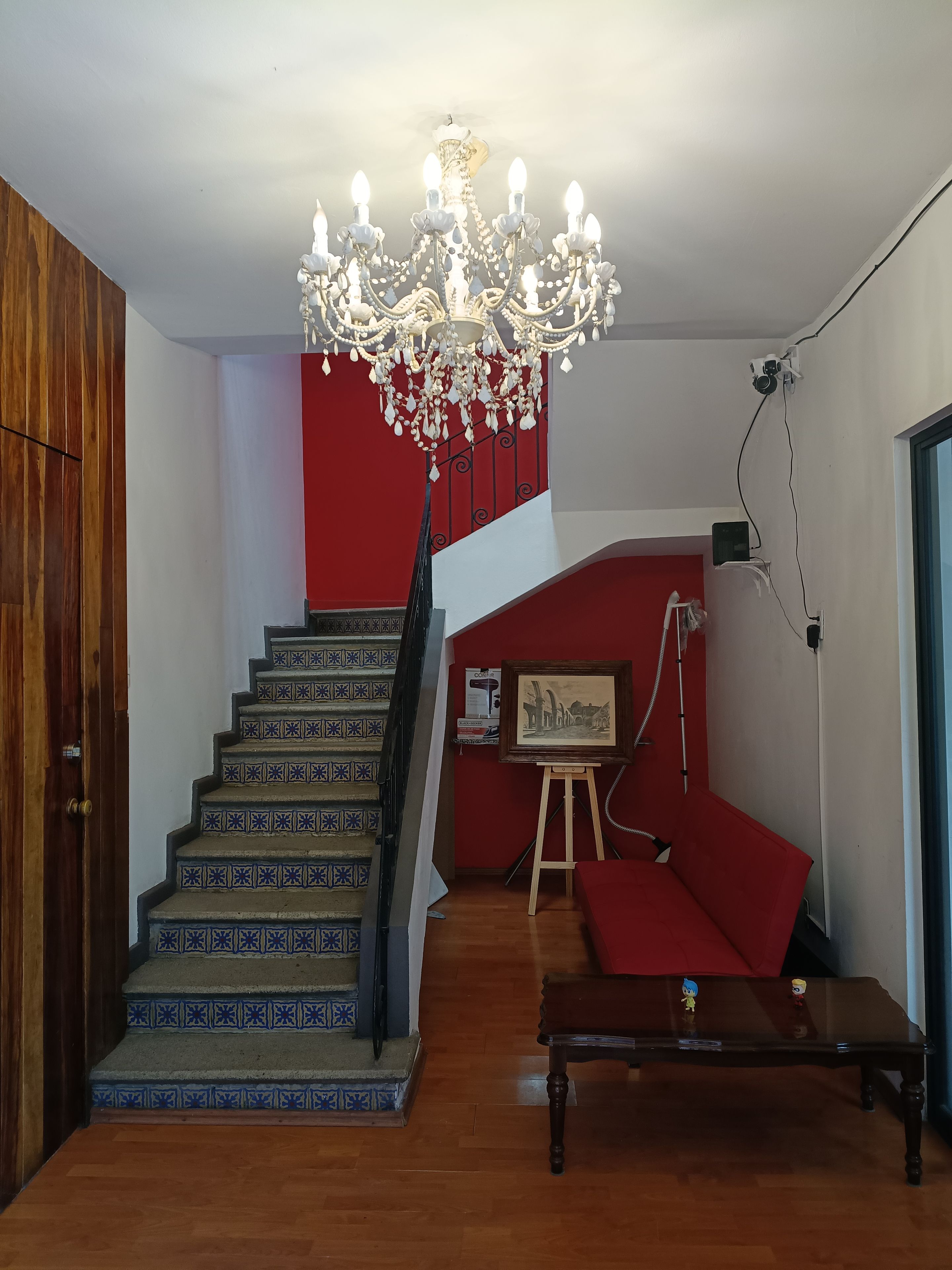 A staircase with patterned steps leading to a red wall, a chandelier, and a small table with figurines.