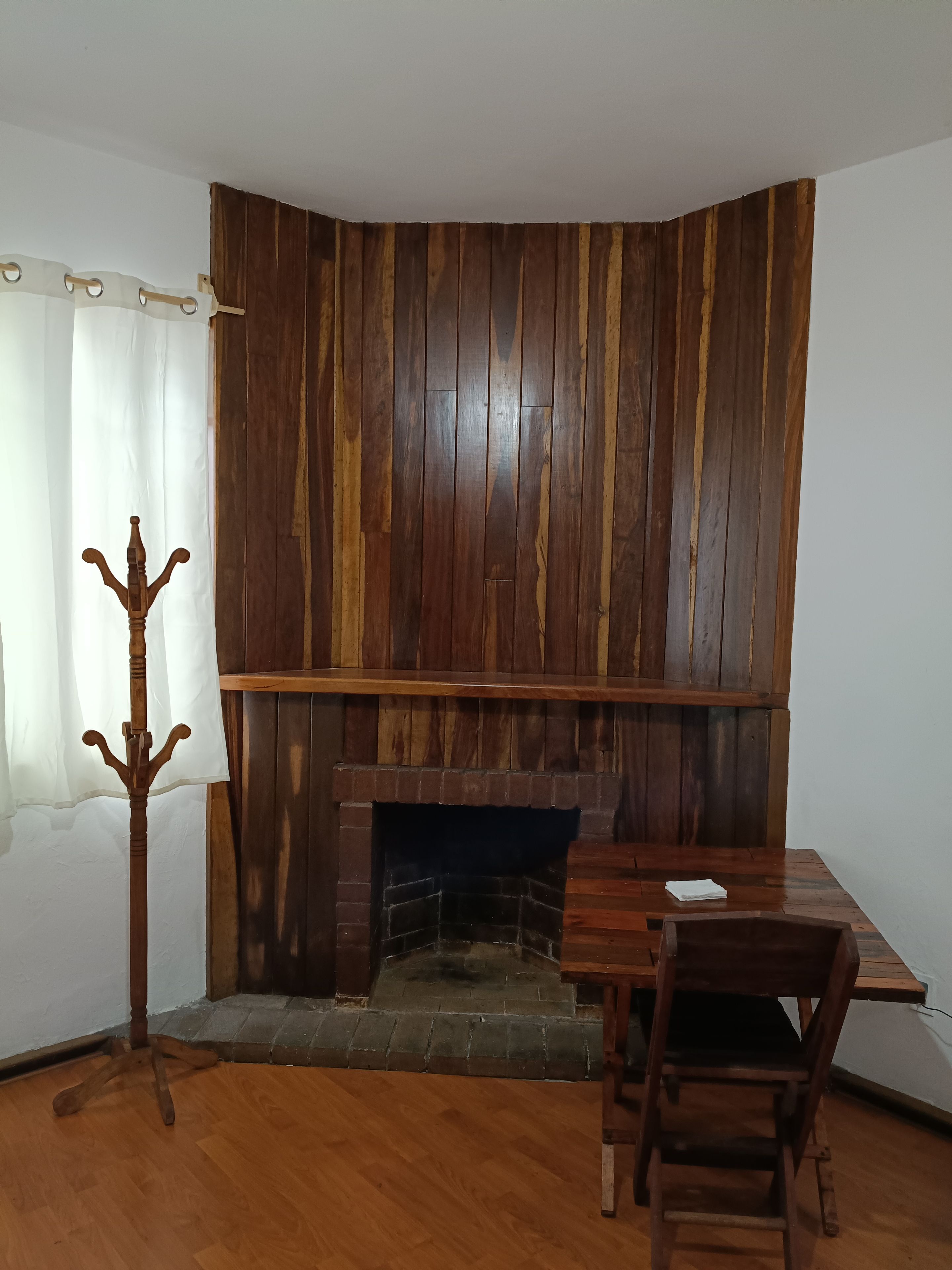 A room with a wooden wall, a fireplace, a dining table, and a coat rack.