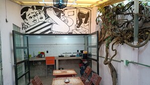 A small outdoor dining area with a tiled floor, wooden tables and chairs, and a mural on the wall. - House Santy Co-Living Condesa (Ciudad de México)