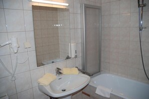 A bathroom with a sink, mirror, towel rack, and a shower area. - Hotel Kuchlerwirt (Treffen)