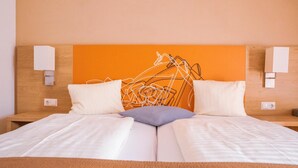 Habitación de hotel con una cama, dos almohadas, cabecero e iluminación empotrada en la pared.