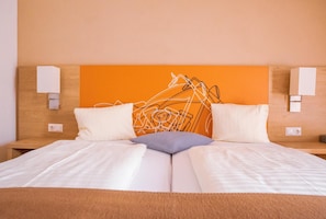Habitación de hotel con una cama, dos almohadas, cabecero e iluminación empotrada en la pared.