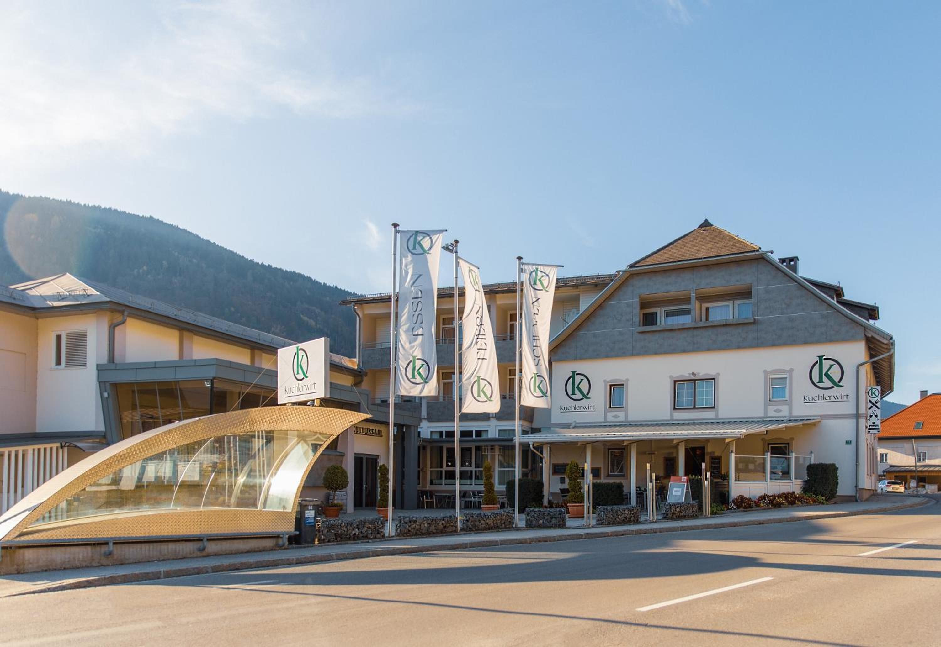 Ein Hotel mit mehreren Flaggen, einem überdachten Eingang und einer Bergkulisse im Hintergrund.