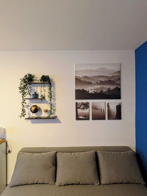 Una habitación con un sofá gris, una estantería empotrada con plantas y adornos, y una serie de fotografías enmarcadas que muestran paisajes.
