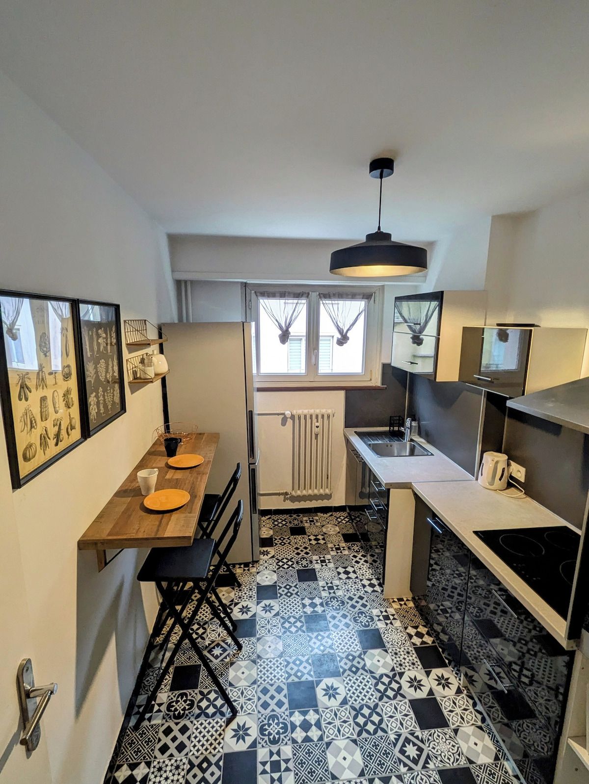 A compact kitchen with a dining area, a radiator, and a window with curtains.