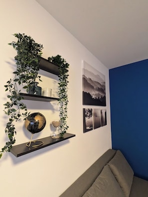 A room with a blue accent wall, a black shelf with decorative plants, a globe, and framed photographs. - Appartement cosy proche du centre de Strasbourg (Strasbourg)