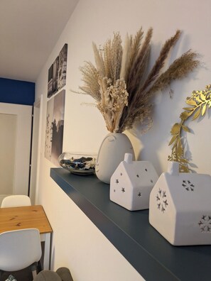 A dining area with a white wall, a blue accent wall, and a shelf with decorative items including a vase with dried plants and star-shaped vases. - Appartement cosy proche du centre de Strasbourg (Strasbourg)