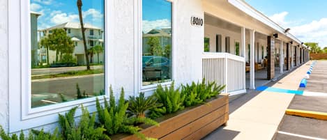 A hotel with a row of rooms, a covered outdoor seating area, and a parking lot.
