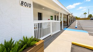 Un hôtel à la façade blanche, portant le numéro 8010, doté d’un espace extérieur couvert avec une rambarde et un jardinier agrémenté de plantes vertes.