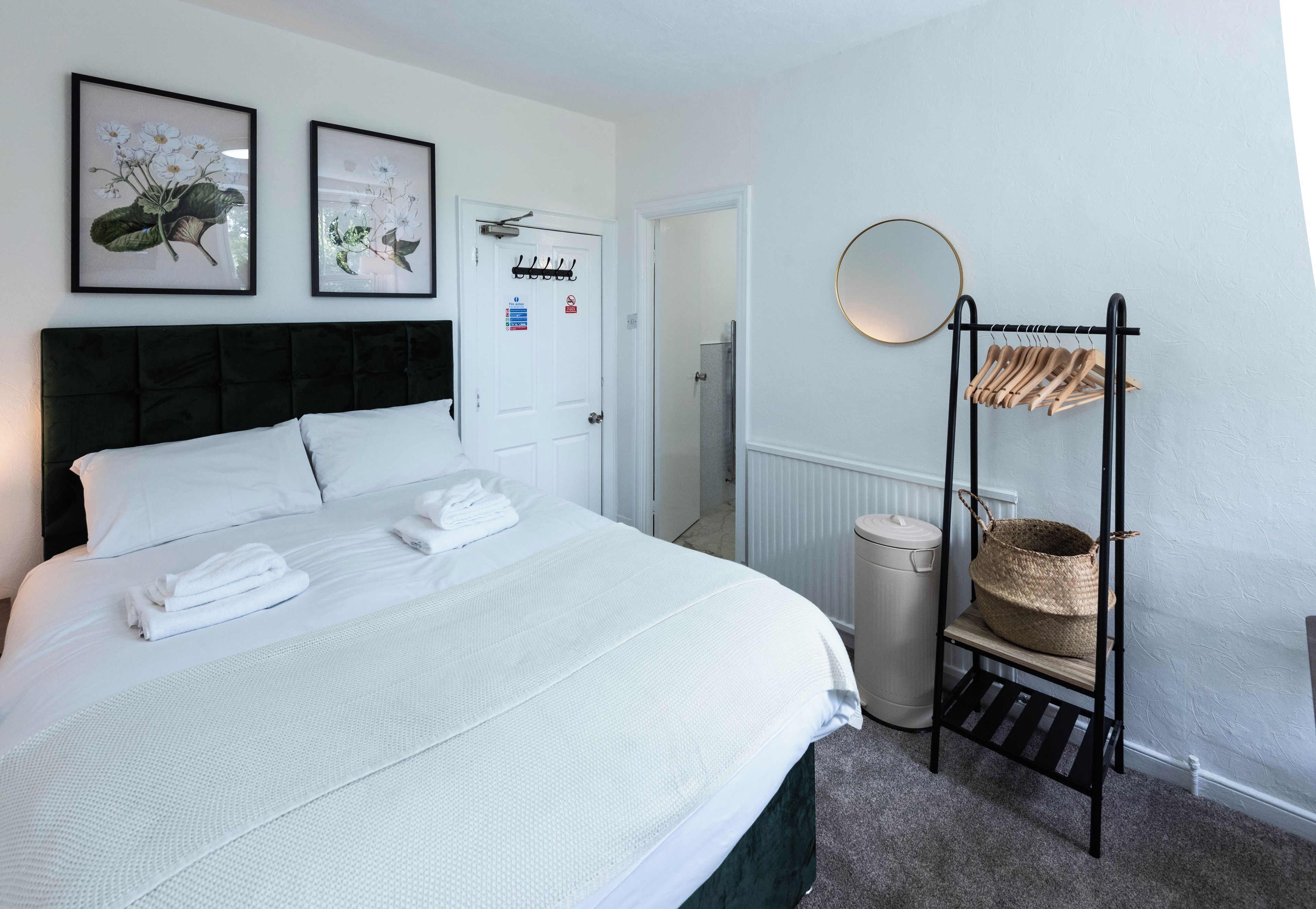 A neatly made bed with white linens and towels, a black headboard, and two framed botanical prints on the wall.