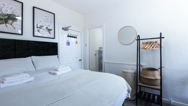 Quarto de hotel com cama, cabideiro, espelho e quadro decorativo com flores na parede.