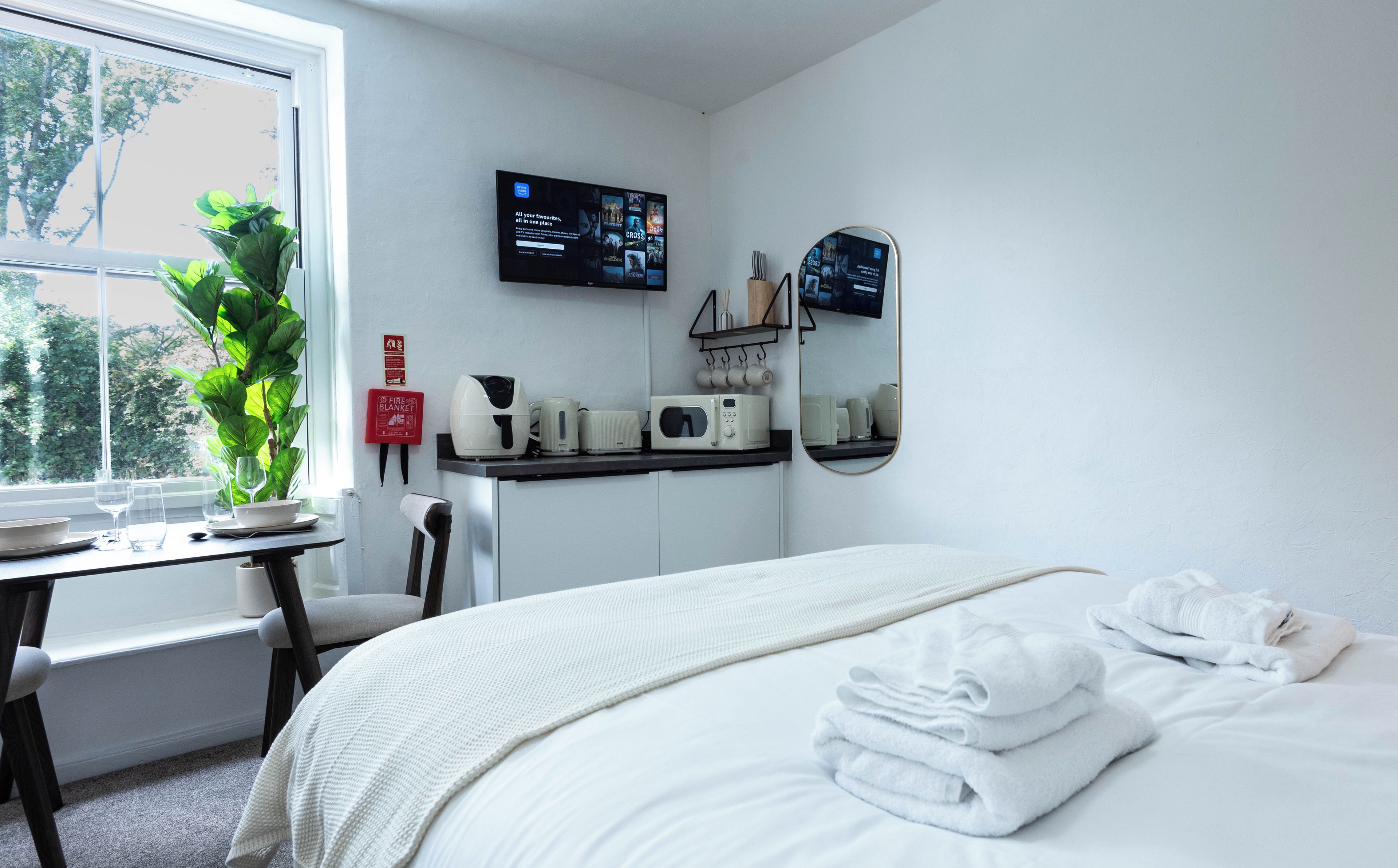 A hotel room with a bed, a desk with a computer, a coffee maker, and a fire extinguisher.
