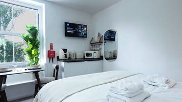 A hotel room with a bed, a desk with a computer, a coffee maker, and a fire extinguisher.