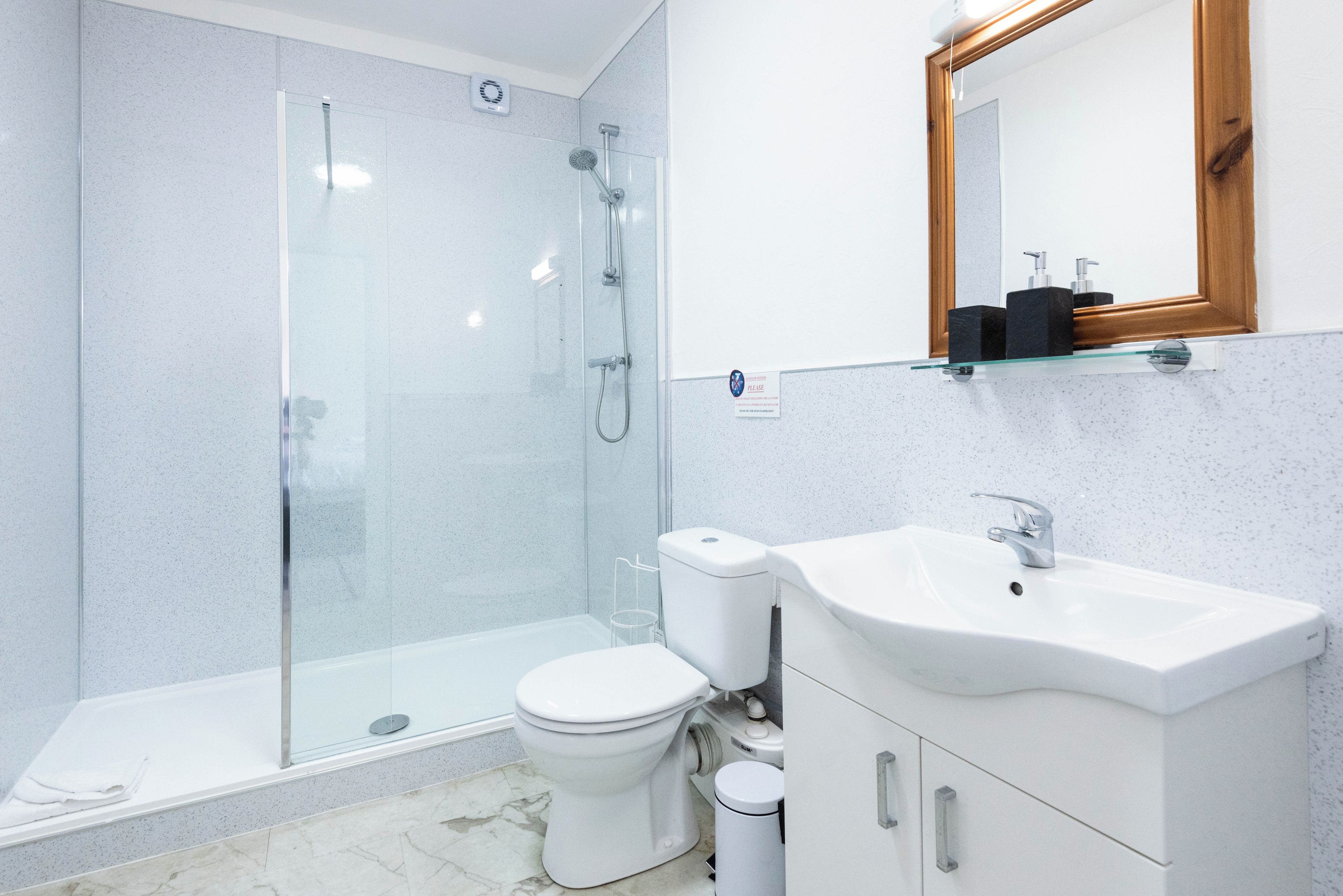 Un baño moderno con ducha de vidrio, inodoro blanco y lavamanos con mueble de madera.