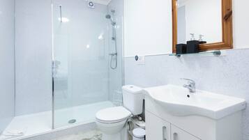 Un baño moderno con ducha de vidrio, inodoro blanco y lavamanos con mueble de madera.