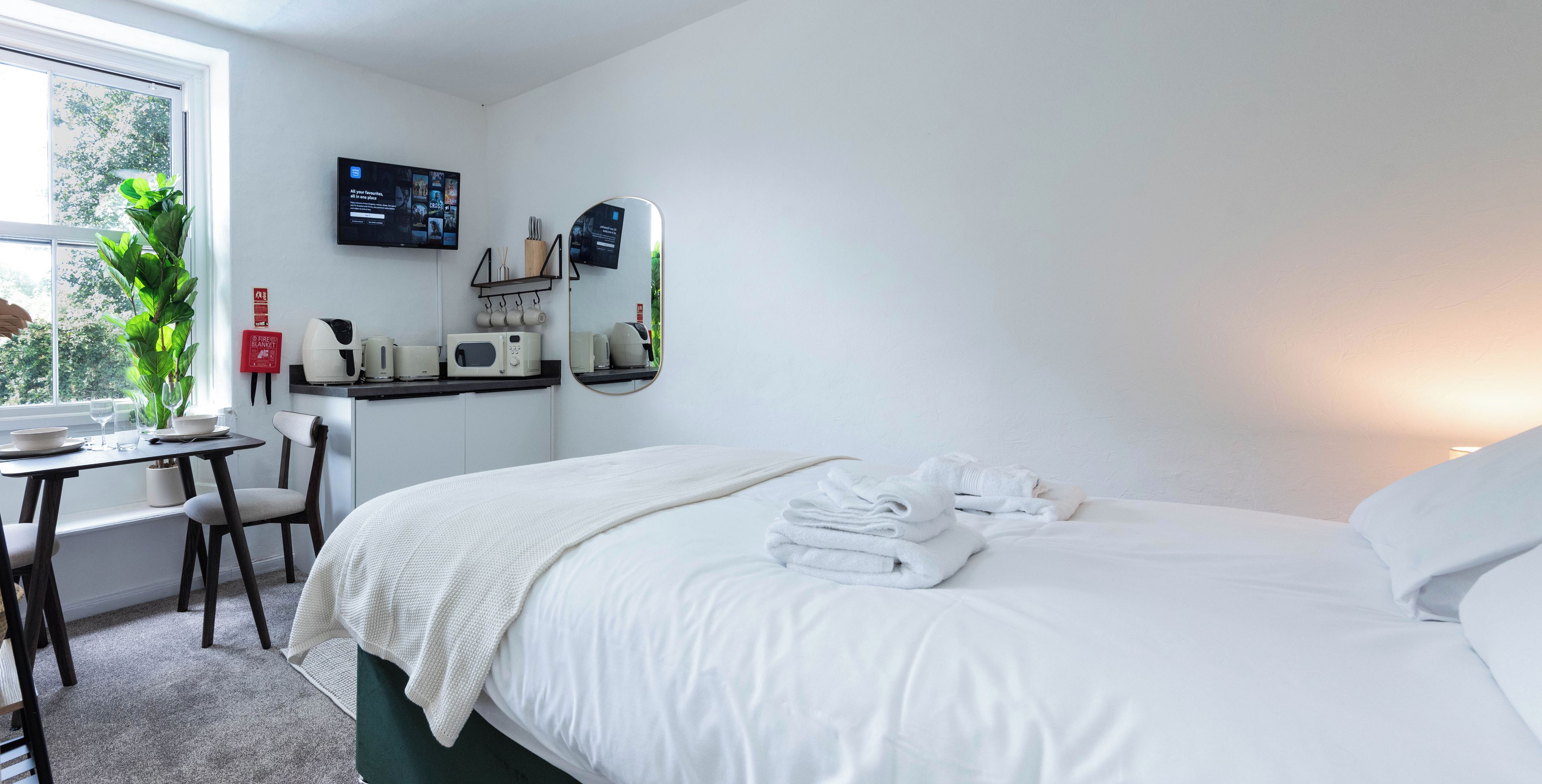 Una habitación de hotel con cama, escritorio con computadora, silla, ventana y planta.