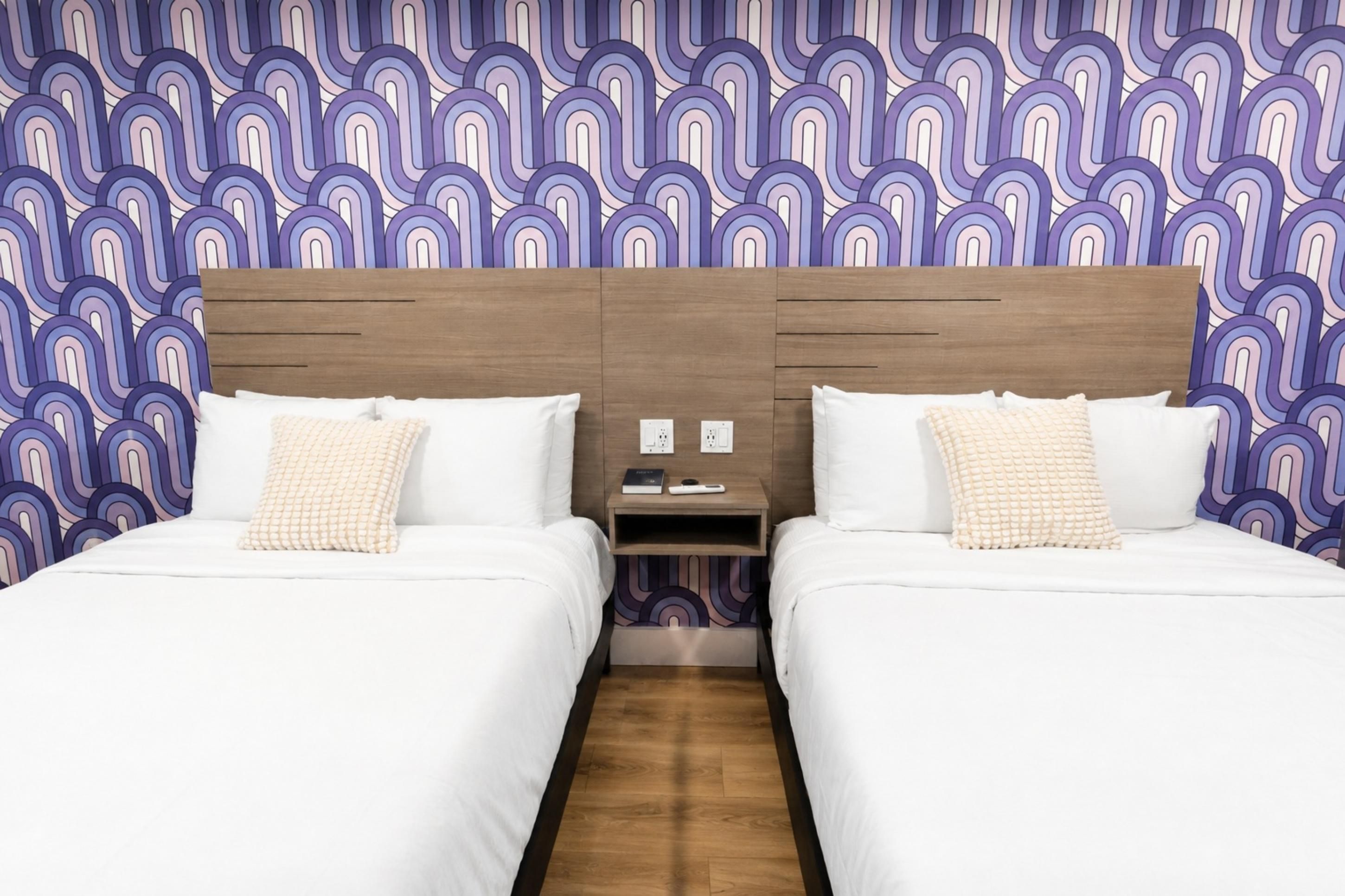 A hotel room with two beds, wooden headboards, and a patterned wallpaper.
