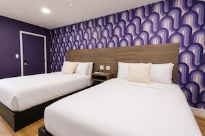 Habitación de hotel con dos camas, cabecero de madera, mesita de noche y pared con estampado.