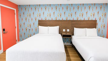 Une chambre d’hôtel avec deux lits, une tête de lit en bois, du linge de lit blanc et un mur orné d’un motif représentant des nageurs.