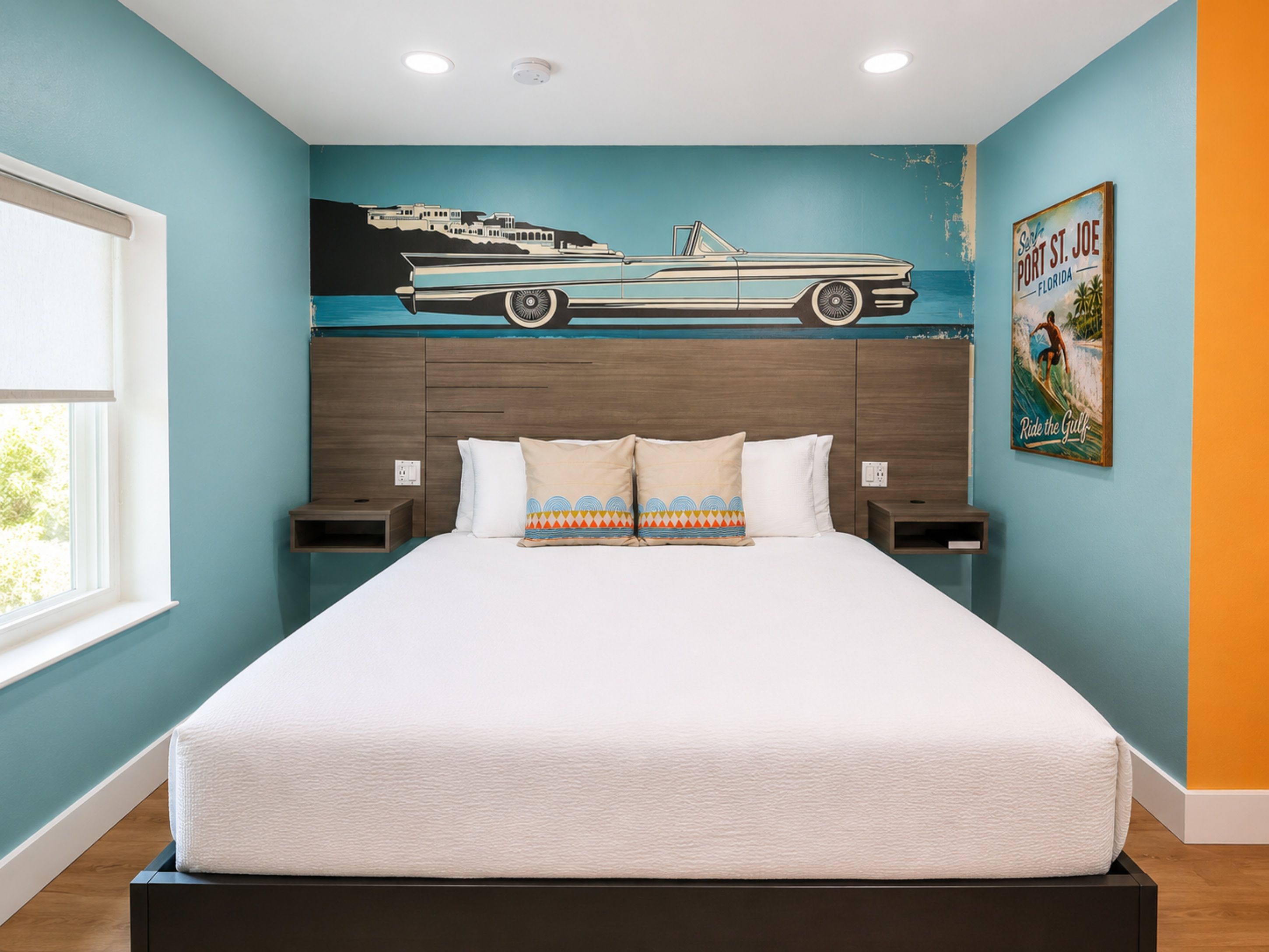 Une chambre à coucher avec un lit, deux tables de chevet, une fresque murale représentant une voiture et une affiche.