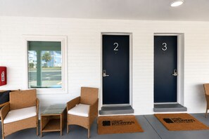 Ein Hotelzimmer mit zwei Türen, mit den Nummern 2 und 3, einem kleinen Tisch mit einem Stuhl und einem an der Wand befestigten Feuerlöscher.