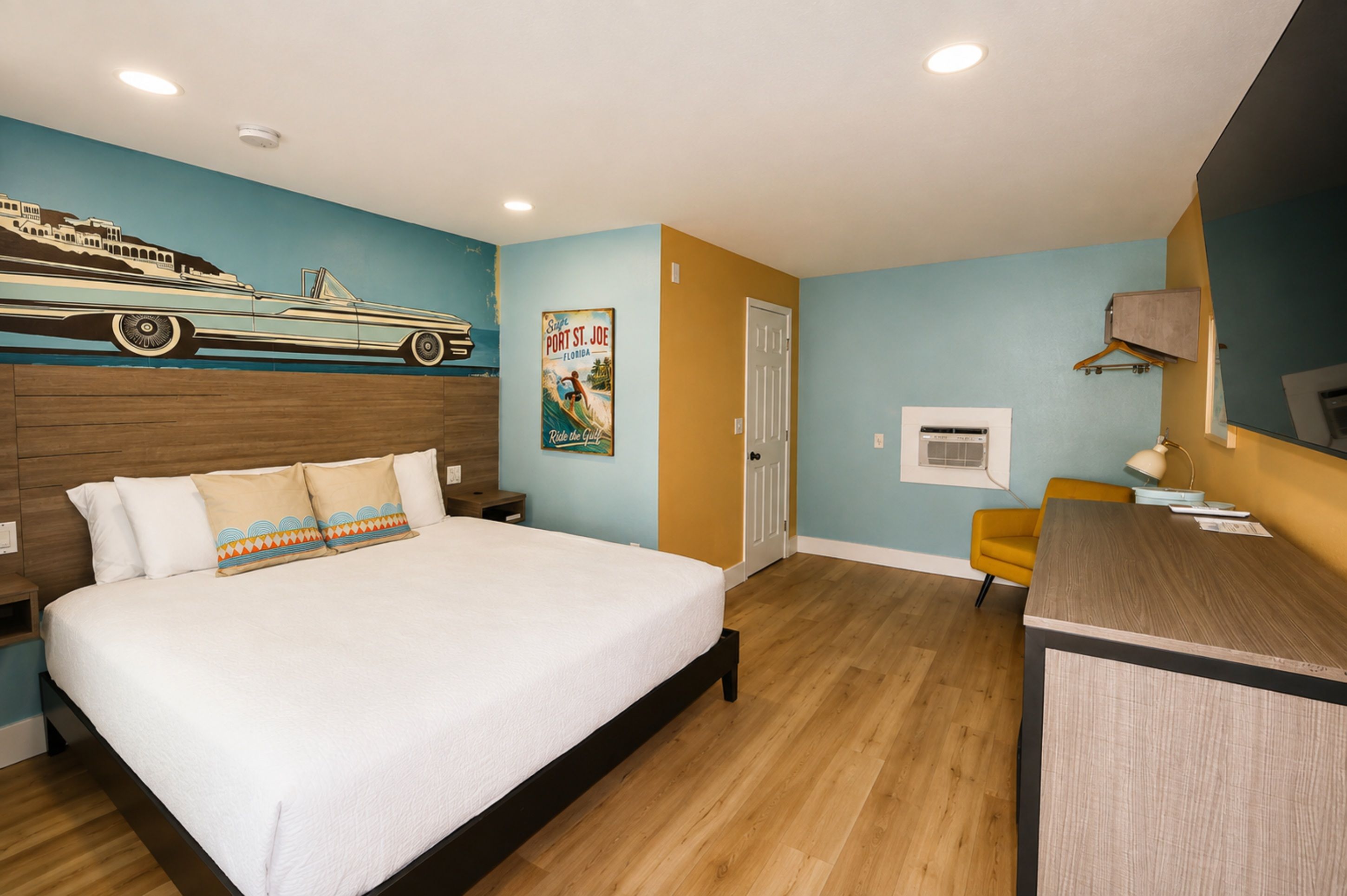 Une chambre d’hôtel avec un lit, un bureau, une chaise, une affiche et un mur orné d’une fresque.