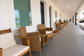 Eine Reihe aus Korbstühlen und Tischen in einem überdachten Gang mit Türen, die mit den Nummern 2 und 3 gekennzeichnet sind.