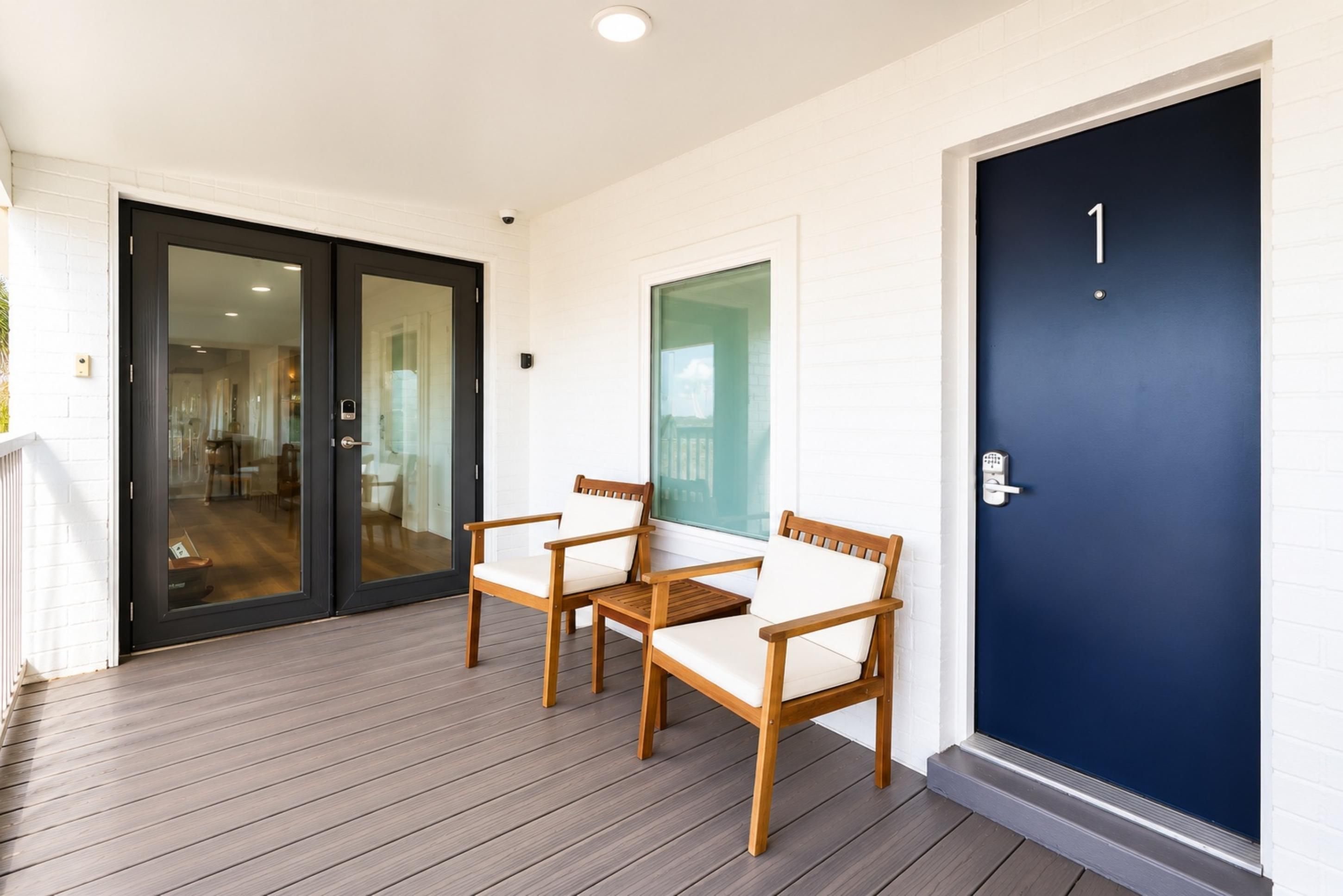 A wooden deck with two chairs and a door with a keypad lock.