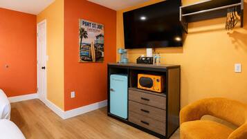 Habitación con paredes anaranjadas, un televisor montado en la pared, un refrigerador pequeño, un microondas, una cafetera y una silla.