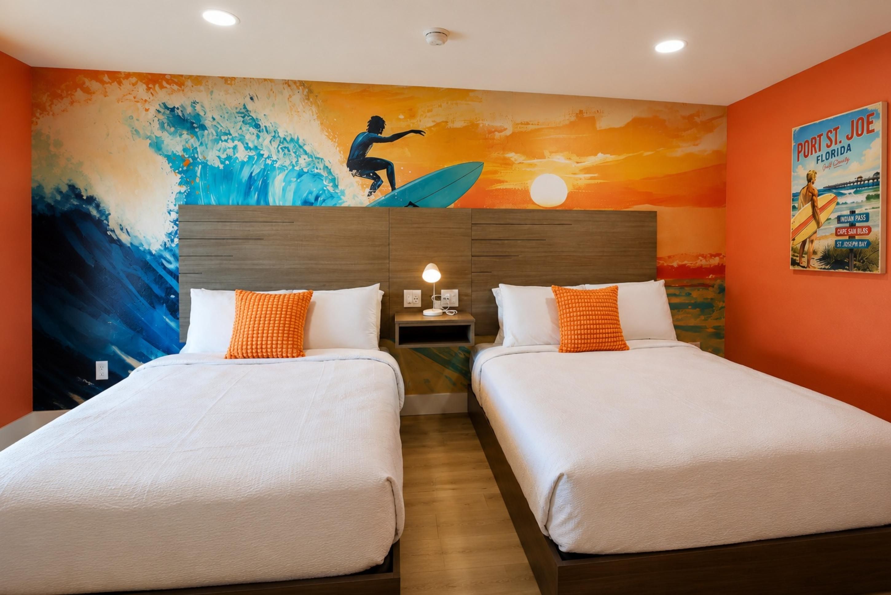 A hotel room with two beds, a mural of a surfer, and a poster on the wall.