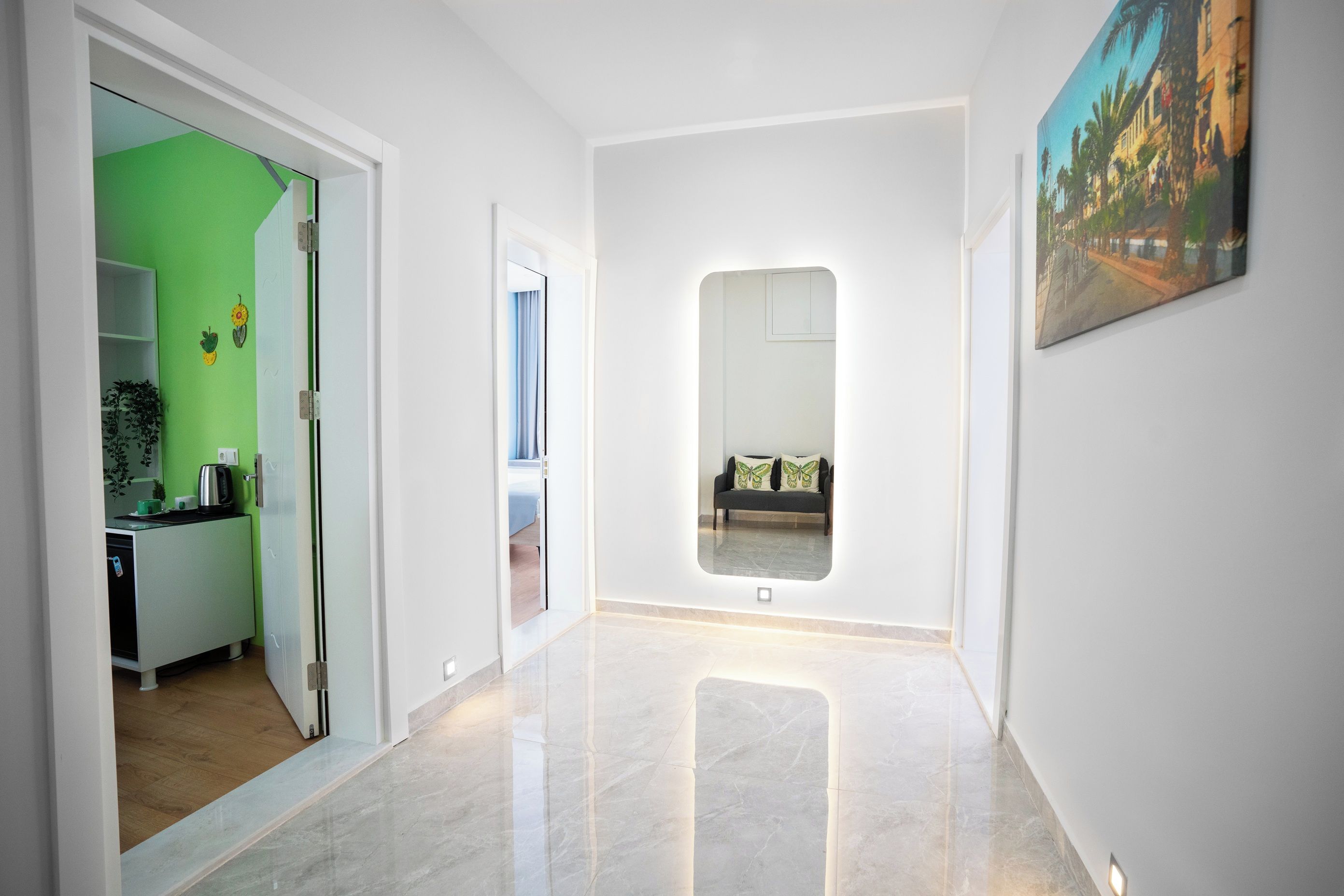A hallway with a mirrored wall, a painting, and a glimpse of a room with a bed and a window.