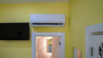 A bathroom with a white air conditioner, a black television mounted on the wall, and a door leading to a bathroom with a marble sink.