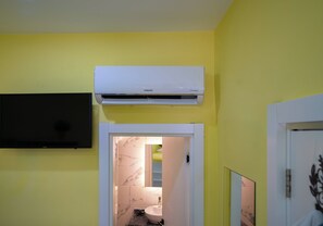 A bathroom with a white air conditioner, a black television mounted on the wall, and a door leading to a bathroom with a marble sink.