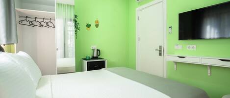 Une chambre d’hôtel équipée d’un lit, d’une télévision, d’un climatiseur, d’un porte-manteau et d’une petite table avec une bouilloire.