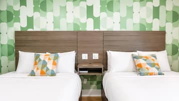 A hotel room with two beds, each with a patterned pillow, a wooden headboard, and a nightstand with a power outlet.