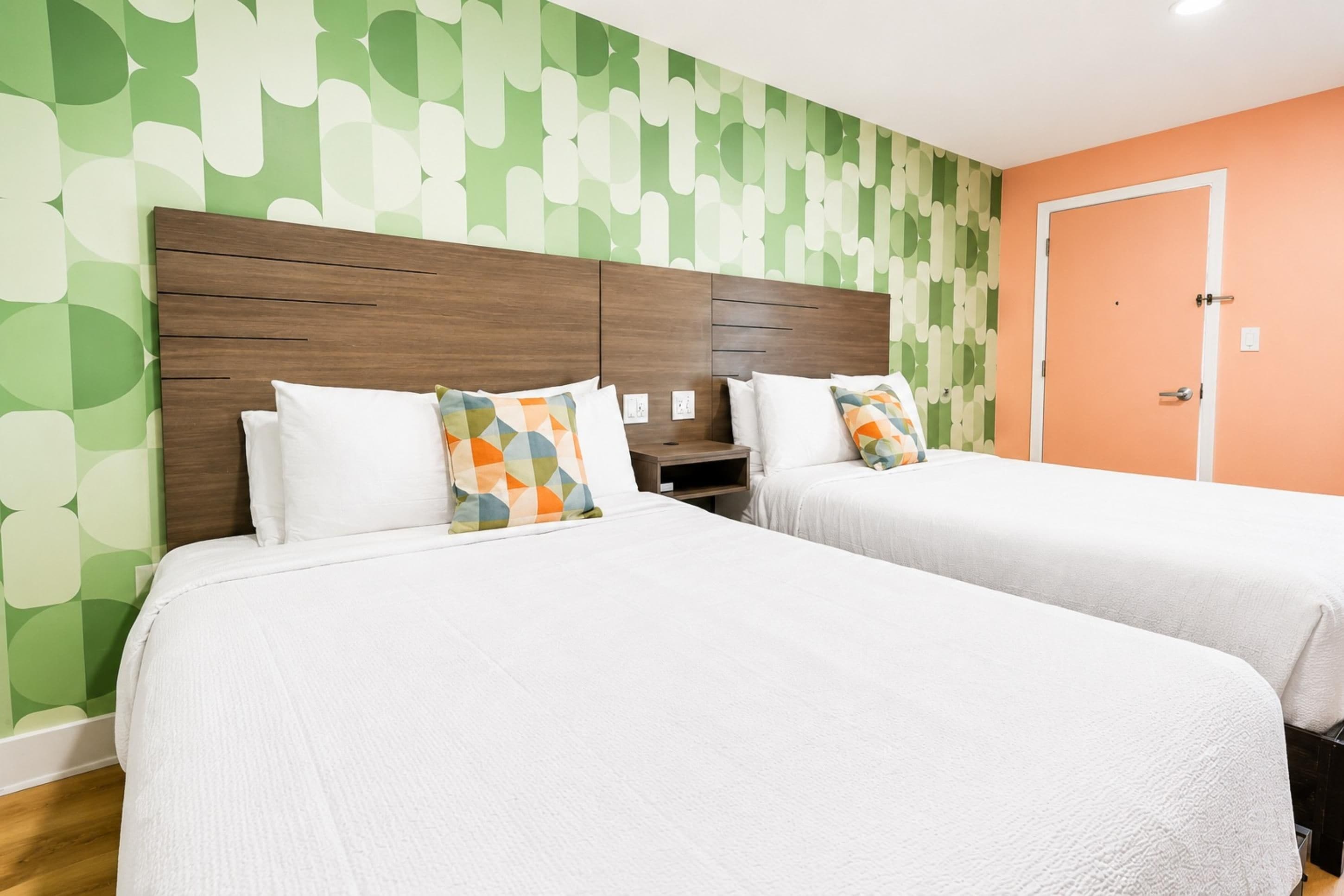 Habitación de hotel con dos camas, cabecero de madera y pared con estampado verde.