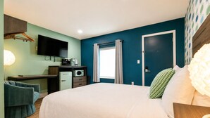 Une chambre à coucher avec un lit, un bureau, une télévision et une fenêtre avec des rideaux.