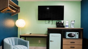 Une chambre dotée d’un téléviseur à écran plat fixé au mur, d’un petit réfrigérateur, d’un four à micro-ondes, d’une machine à café et d’une chaise.