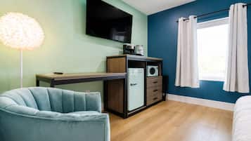 Habitación compacta con cama, escritorio, silla, televisor de pantalla plana, cafetera y microondas.