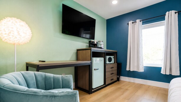 Une chambre compacte comprenant un lit, un bureau, une chaise, un téléviseur à écran plat, une machine à café et un four à micro-ondes.