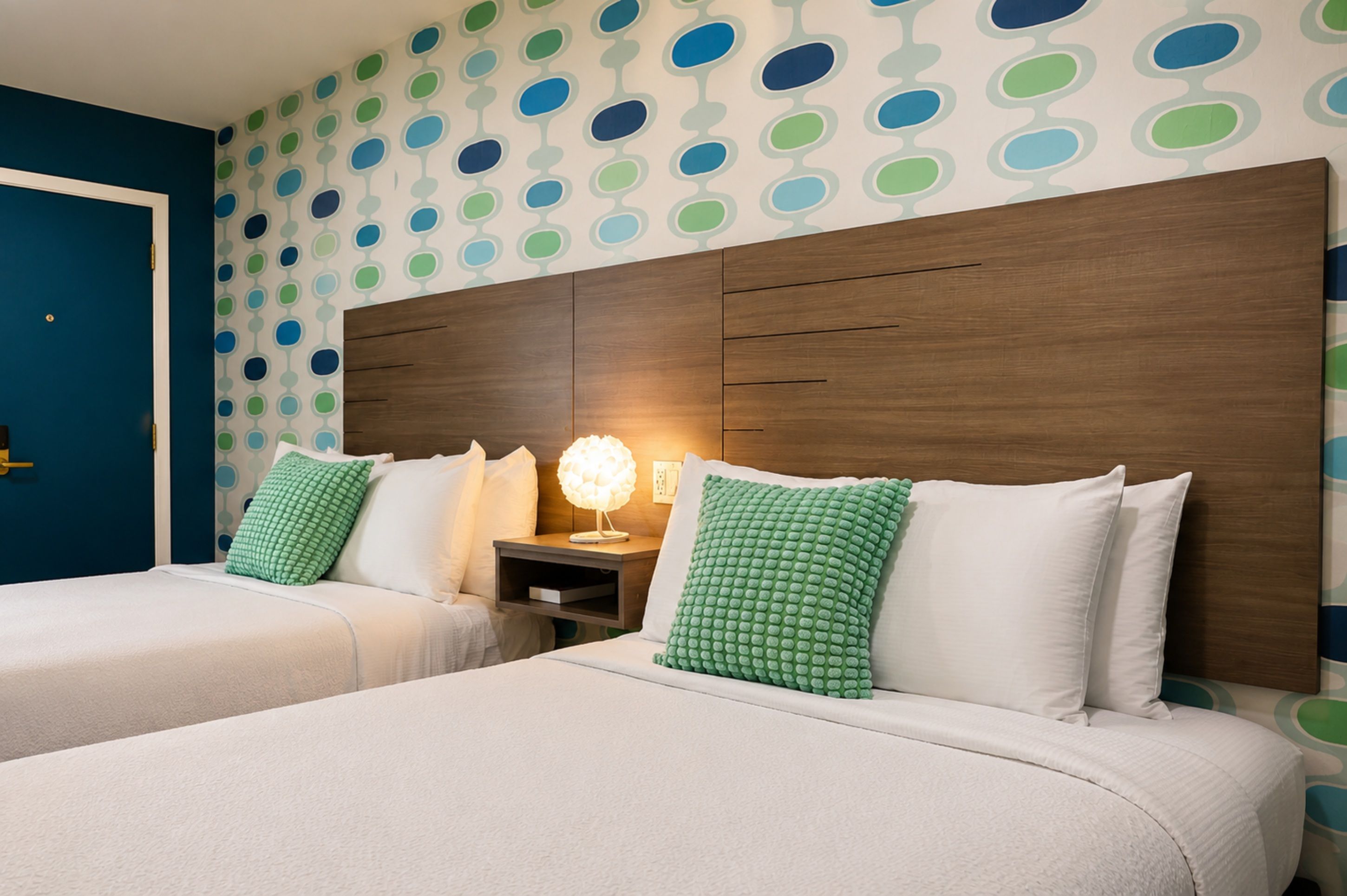 A hotel room with two beds, a nightstand, and a wall with a polka dot pattern.