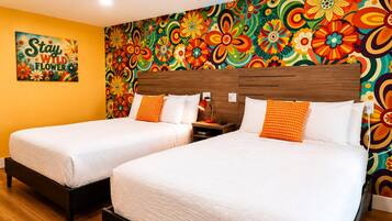 A hotel room with two beds, a colorful floral wall mural, and a sign that reads 'Stay Wild Flowers'.