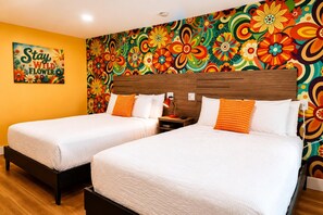 Et hotelværelse med to senge, et farverigt blomstermotiv på væggen, og et skilt med teksten 'Stay Wild Flowers'.