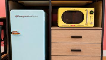 Un refrigerador azul con el nombre de marca 'Frigidaire' y un microondas amarillo de estilo retro sobre un gabinete de madera con cajones.