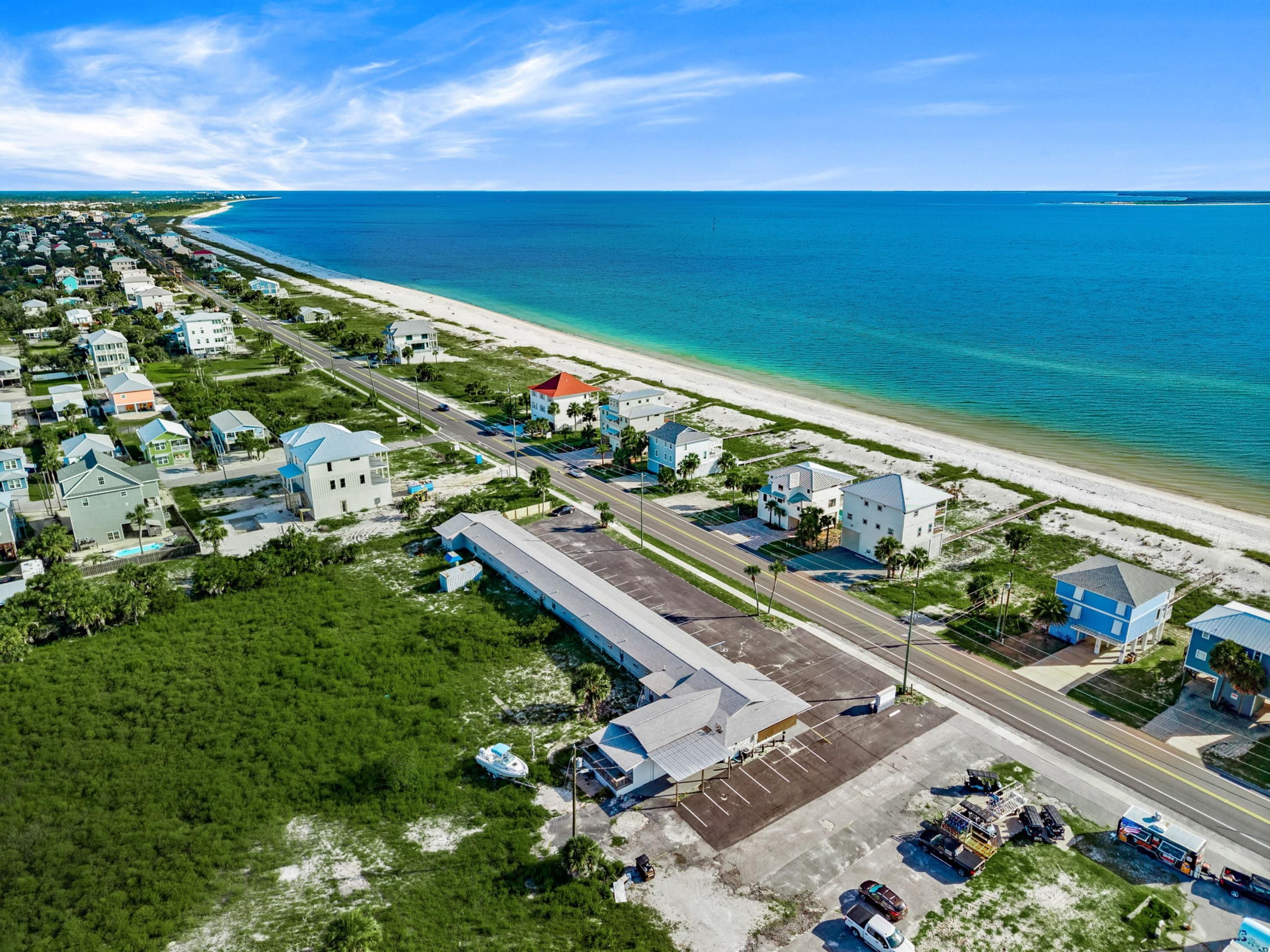 An aerial view of a coastal residential area with houses, a beach, and a clear sky.