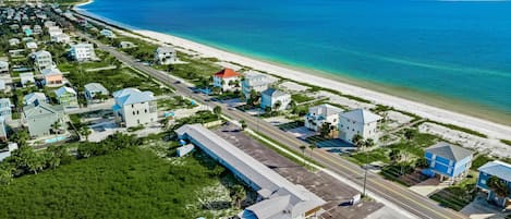An aerial view of a coastal residential area with houses, a beach, and a clear sky.