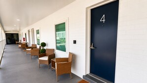 Corredor de hotel com uma fileira de cadeiras de vime e uma porta azul escura identificada com o número 4.