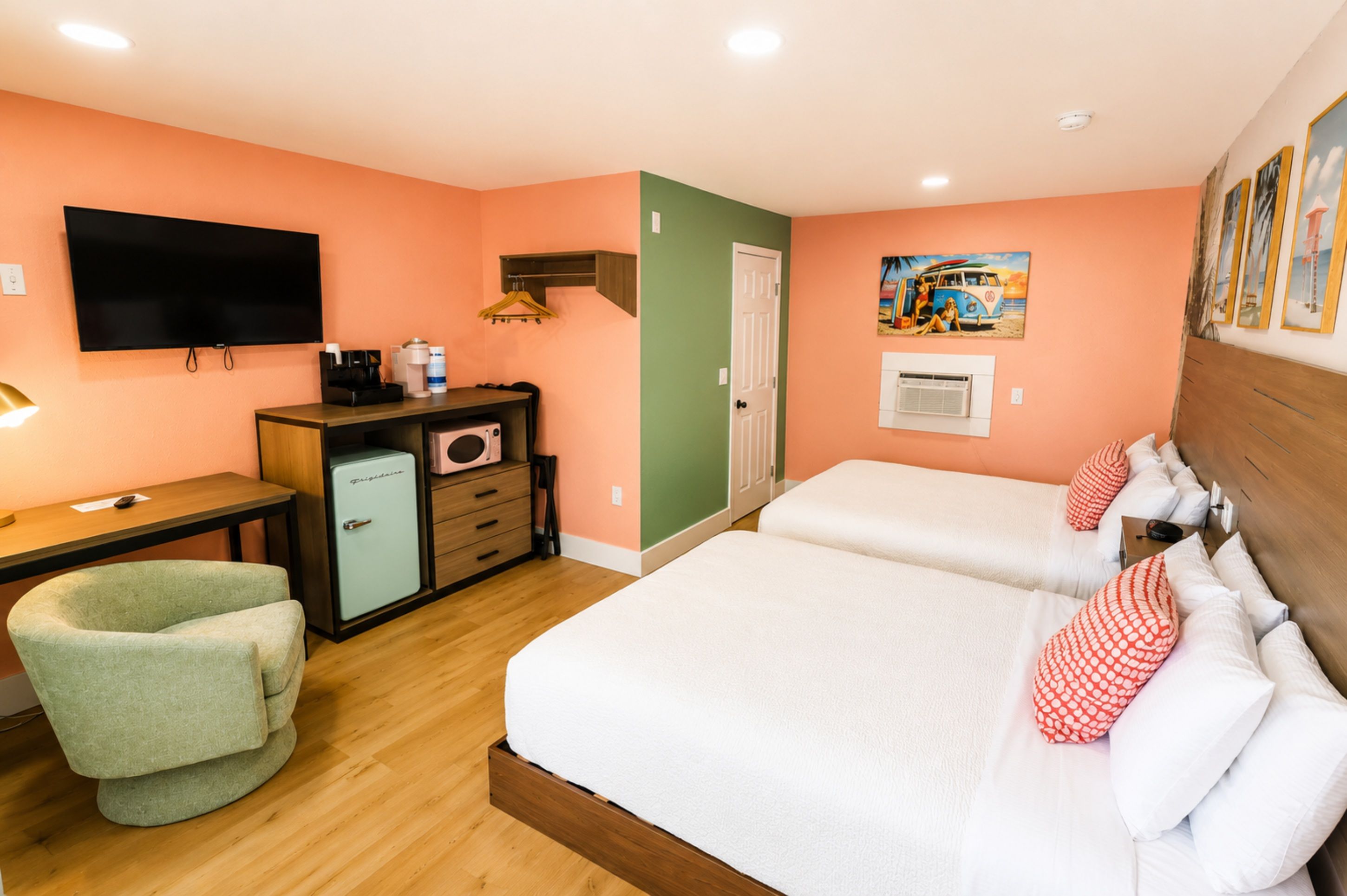 Habitación de hotel con cama, escritorio, silla, refrigerador, televisor y un cuadro en la pared.