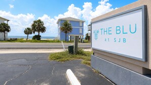 Placa de 'The Blu at Sub' com vista para uma praia e palmeiras ao fundo.