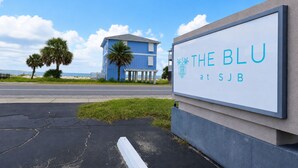 Une enseigne indiquant « The Blu at SJB », avec en arrière-plan un bâtiment bleu et des palmiers.